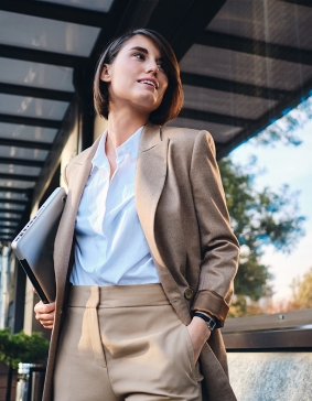 Frau steht im Blazer mit Laptop unter dem Arm